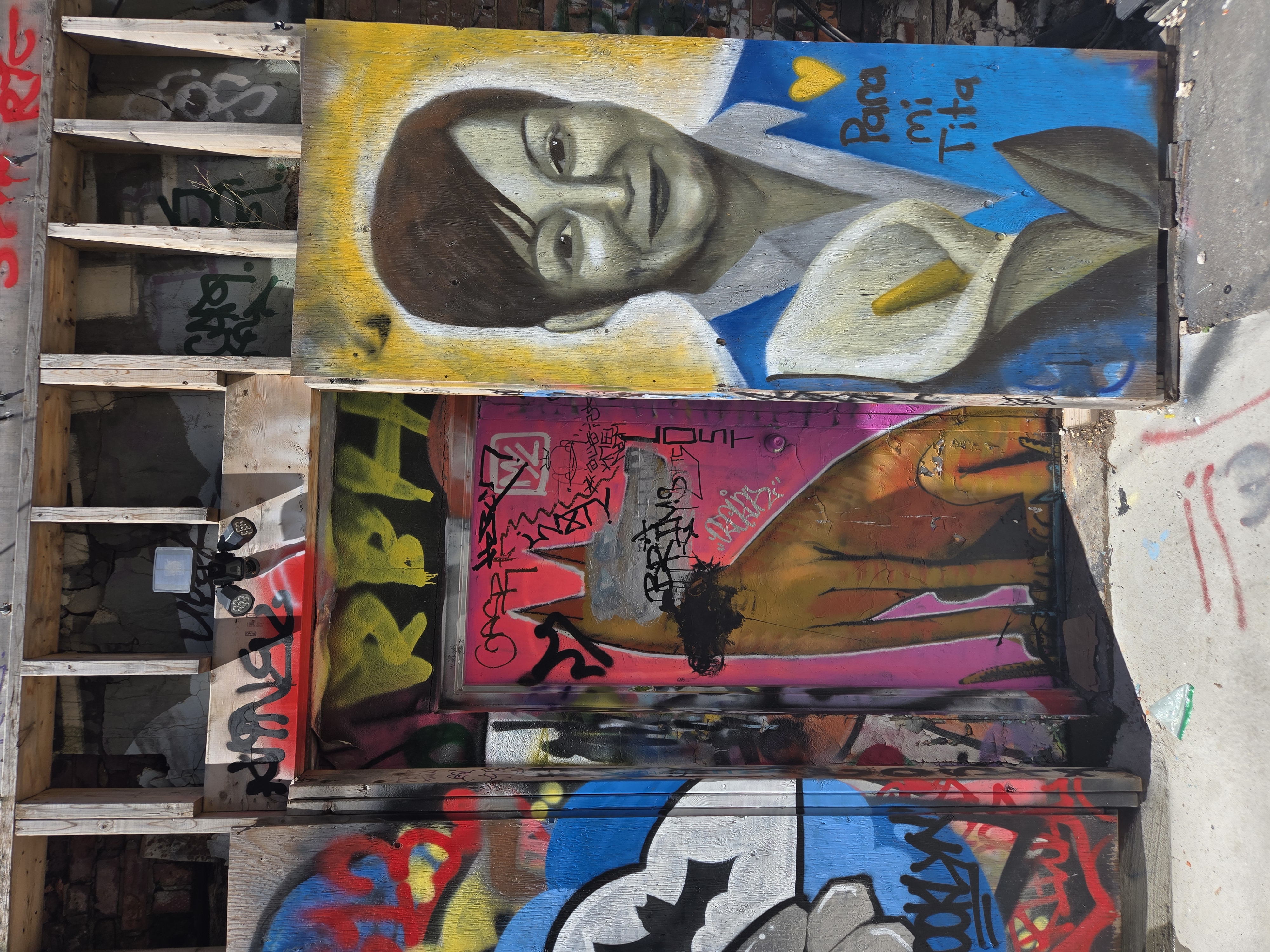Two murals in a Kensington back alley — a haloed portrait titled Para mi Tita beside a reclining figure layered over years of tags.